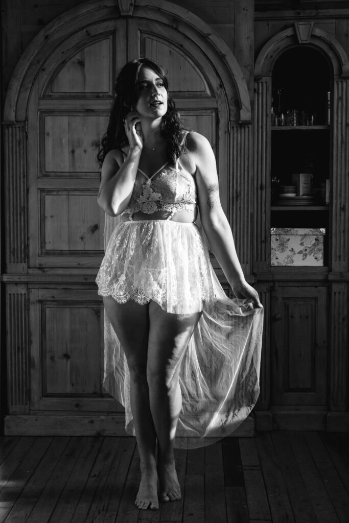 Black and white image of woman in bridal lingerie by a window