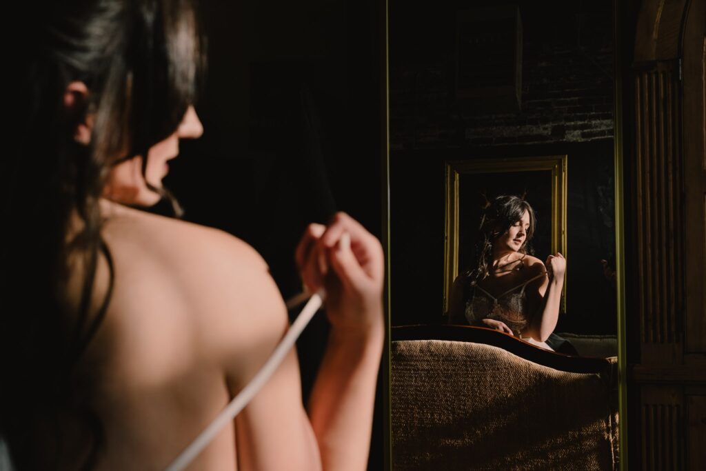 Woman in a mirror removing a lingerie strap in her boudoir photography session