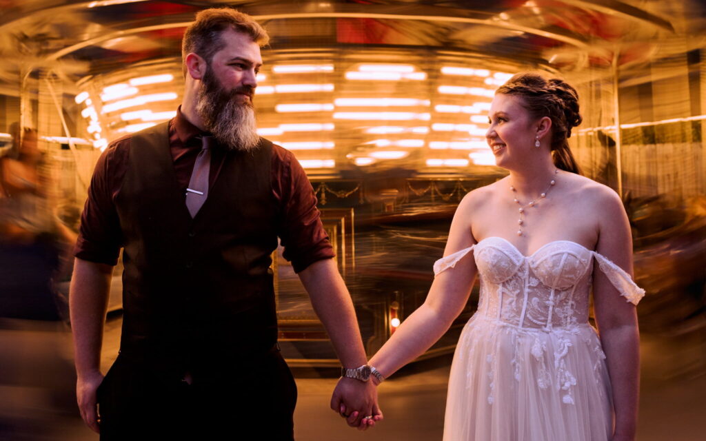 Bride and groom hold hands in front of a carousel at a Knoxville wedding venue