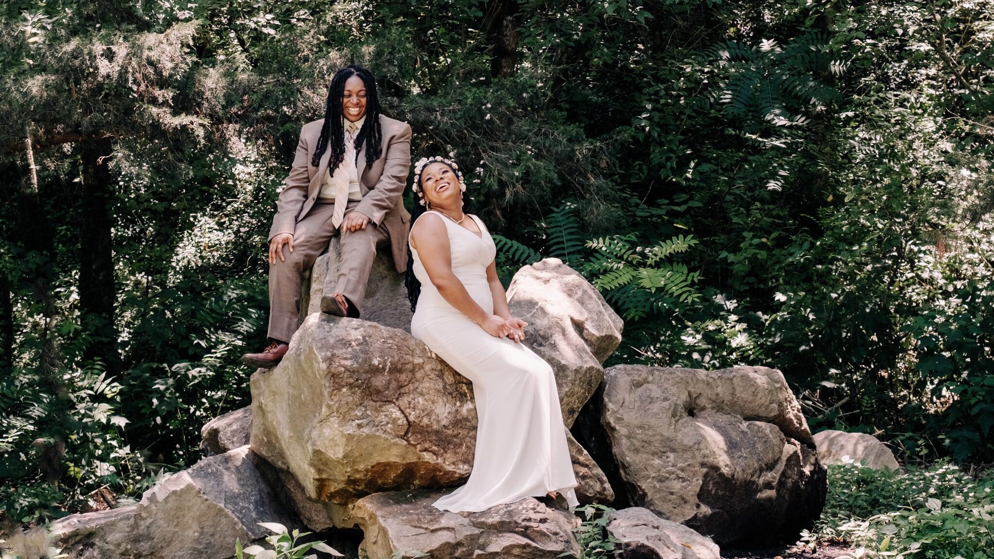Bride and groom laugh at each other while sitting on rocks at an outdoor Knoxville wedding venue